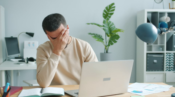 Person sat at desk with laptop looking stressed with head in hands