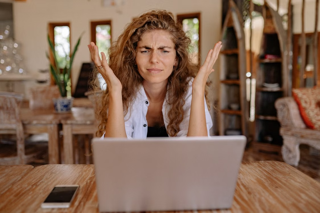 Woman sat at a desk on her laptop looking confused and frustrated