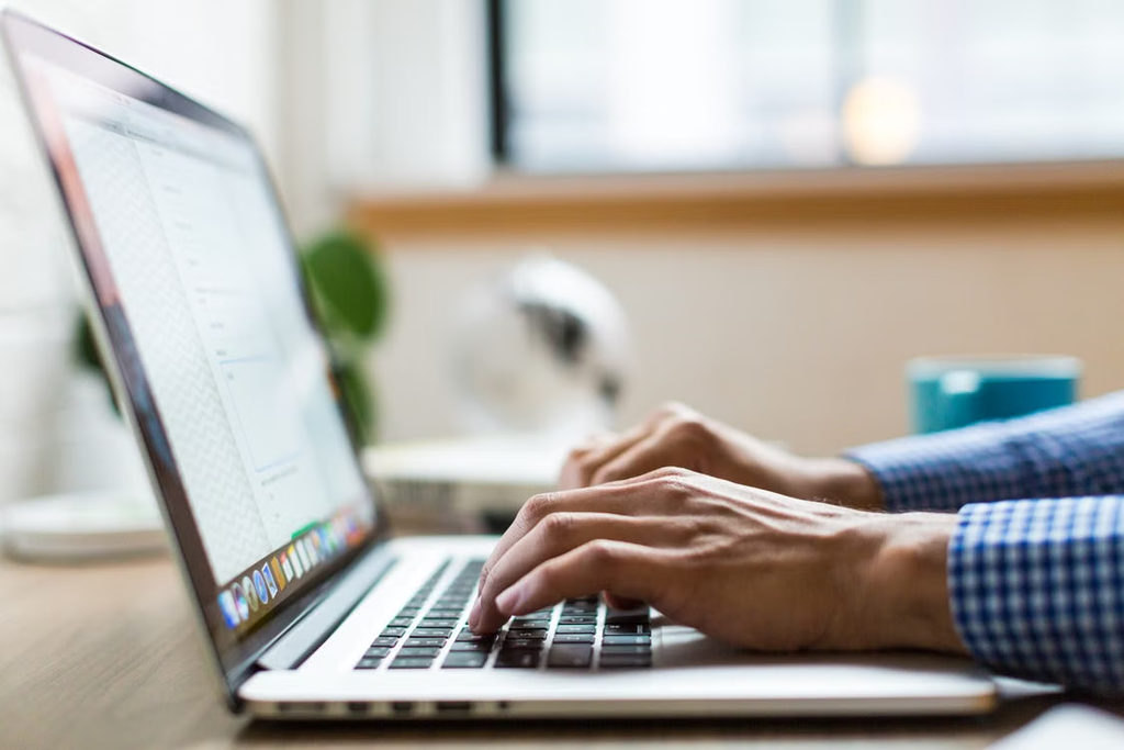 Person sat at a desk working on their laptop looking up 'what are FAQs?'